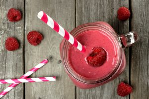 Jay Filled with Raspberry Smoothie Along With Scattered Berries and Straws on Wooden Tab;e | Vitacost.com/blog