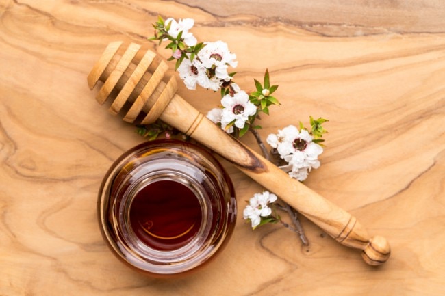 5 Benefits & Uses of Manuka Honey Manuka honey in a glass jar with honey dipper and Manuka flower | Vitacost.com/Blog