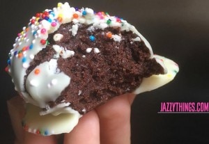 Hand holding up chocolate cake ball with white chocolate icing and sprinkles