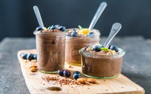 3 jars of chocolate protein pudding with spoons and blueberries on wood cutting board