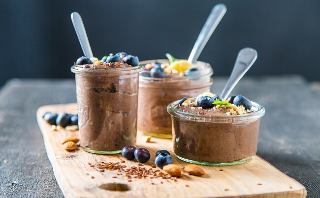 3 jars of chocolate protein pudding with spoons and blueberries on wood cutting board