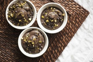 Dark chocolate pudding with crushed pistachio topping in white ramekins