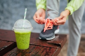 Green detox smoothie cup and woman lacing running shoes before workout on rainy day