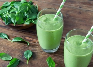 Two green smoothies with spinach leaves on wooden background