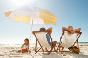 Parents & Kid Relaxing on Beach Under Umbrella for Summer Safety | www.vitacost.com/blog