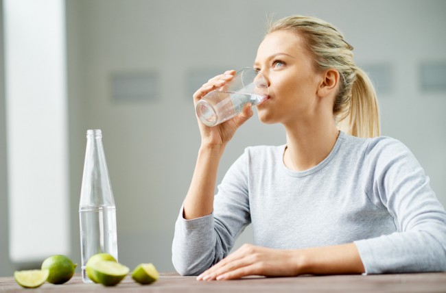 Woman at Table Drinking a Glass of Warm Water | www.vitacost.com/blog