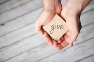 Hands holding cardboard square with the word "give" written on it | Vitacost.com/Blog
