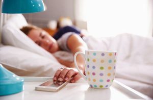 Woman in Bed Suffering From Sleep Loss Pressing Snooze Button on Phone | Vitacost.com/blog