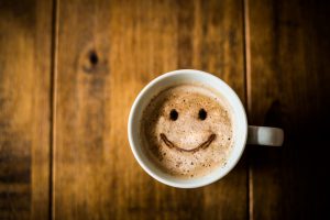 A coffee cup with happy face design in foam on a rustic wood table | Vitacost.com/Blog
