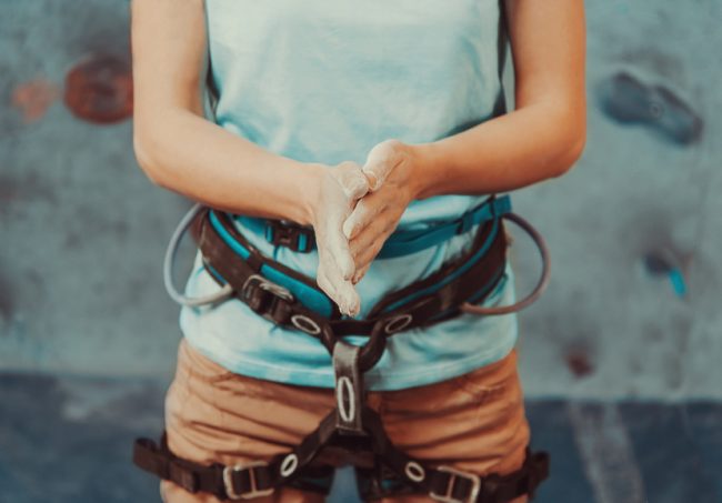 5 Indoor Workouts & Hobbies for Anyone Woman wearing harness, rubbing hands together with chalk before indoor rock climbing | Vitacost.com/Blog