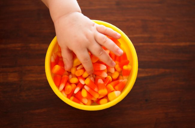 Child at Risk of Eating Too Much Sugar with Hand in Bowl of Candy Corn | Vitacost.com/blog