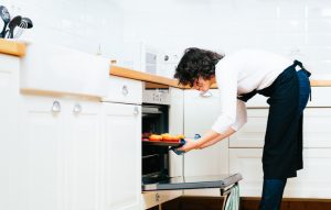 Woman Preparing Thanksgiving Dinner Removing Tray of Baked Goods from the Oven | Vitacost.com/Blog