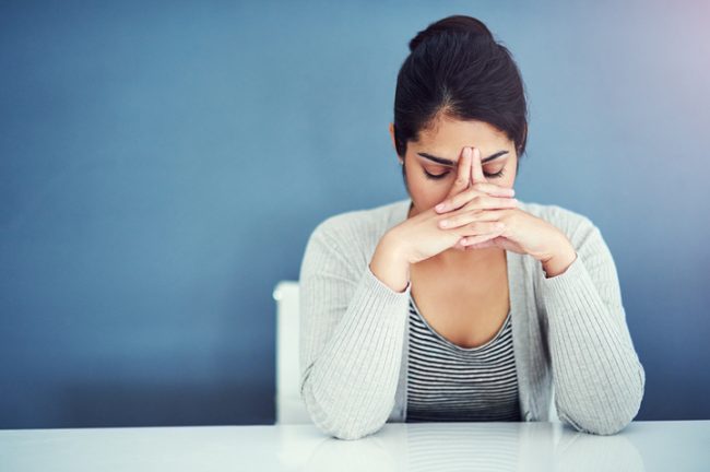 3 Alternative Ways to Cope With Stress & Trauma Woman in Need of Way to Cope With Stress At Table With Hands Over Face | Vitacost.com/blog