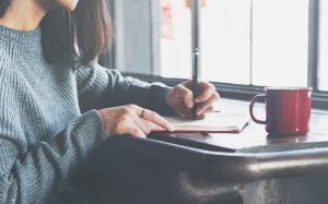 Woman Sitting at Table with Mug of Tea Writing Goals in Journal | Vitacost.com/blog