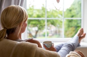 Woman Learning How to Cope With Stress Drinking Tea With Feet Up by Window | Vitaoost.com/blog