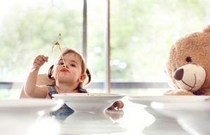 Girl Eating Gluten-Free Pasta at Table With Teddy Bear | Vitacost.com/blog