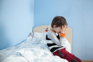 Young Boy in Need of Stress Relief Tips Holding Head Sin Frustration on Bed | Vitacost.com/blog