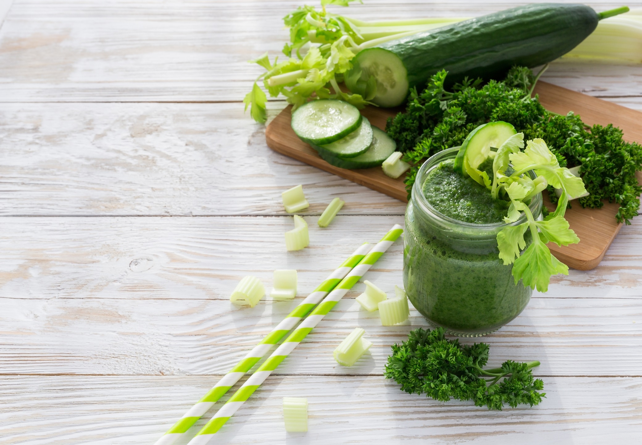 Green Spirulina Smoothie on White-Washed Wood with Straws & Cut Vegetables #recipe | Vitacost.com/blog