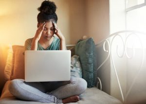 Woman Rubbing Temples With Eyes Closed and Computer in Lap Trying to Reduce Stress | Vitacost.com/blog
