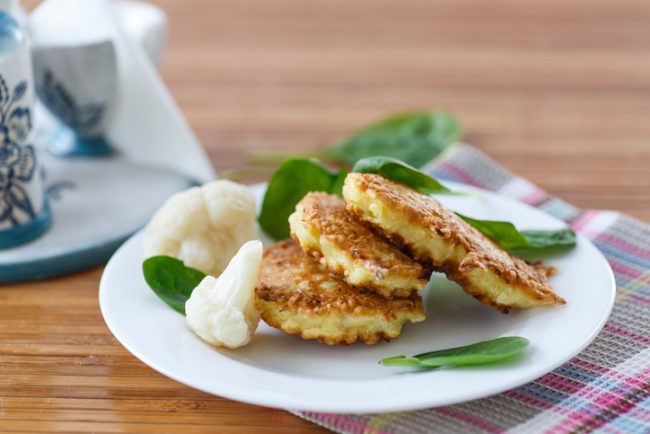 Vegan Recipe: Cheesy Cauliflower Fritters  Cauliflower Fritters on White Plate with Cauliflower Florets & Spinach | Vitacost.com/blog