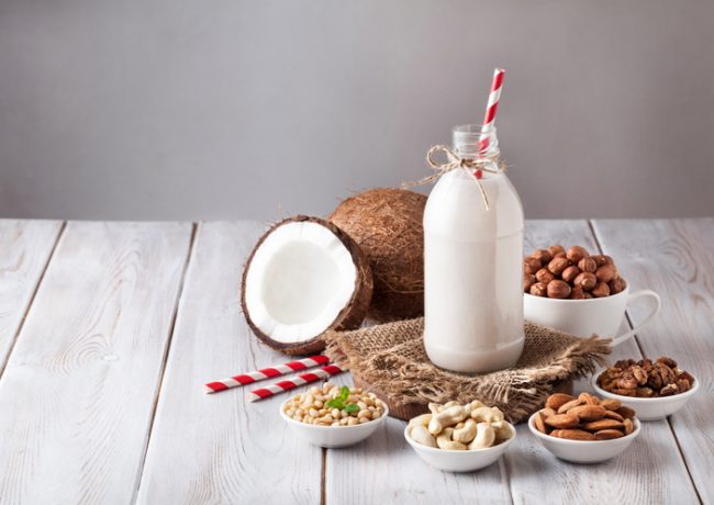 Dairy-Free Milk Substitute in Bottle and Various Nuts on White Wooden Table | Vitacost.com/blog