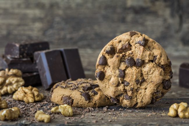 Easy Vegan Chocolate Chip Walnut Cookies  Vegan Chocolate Chip Walnut Cookies on Wood Table with Nut & Chocolate Pieces| Vitacost.com/blog