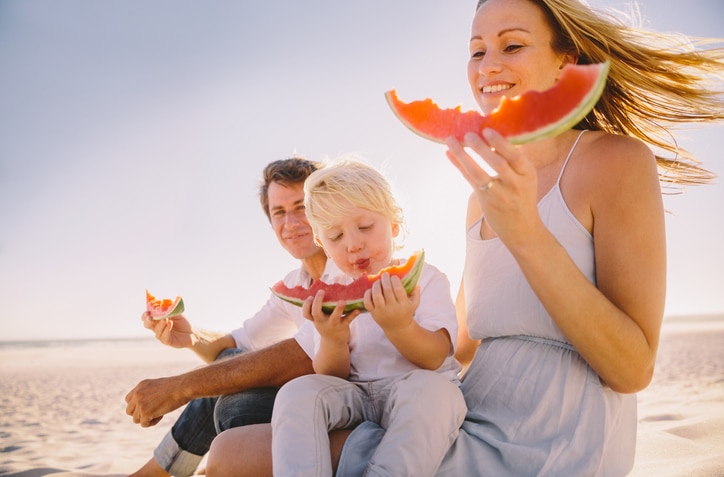 Family Following Gluten-Free Travel Tips Eating Watermelon on the Beach | Vitacost.com/blog