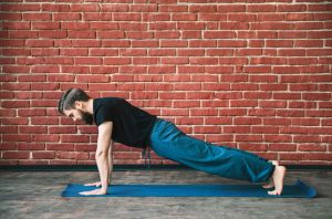 Beaded Guy Practicing Yoga for Men on Blue Mat in Front of Brick Wall | Vitacost.com/blog