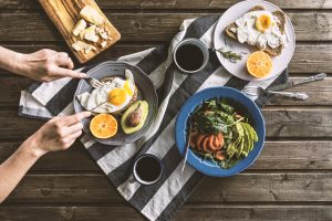 Woman Cuts into Over-Easy Eggs on Toast with Avocado & Orange to Meet Daily Protein Needs | Vitacost.com/blog