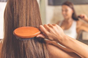 Woman Starting to Get Gray Hair Brushing Her Chestnut Locks in the Mirror | Vitacost.com/blog