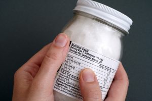 Hand Holds Jar of Coconut Oil with Nutrition Facts Panel: Is it Healthy or Not? | Vitacost.com/blog