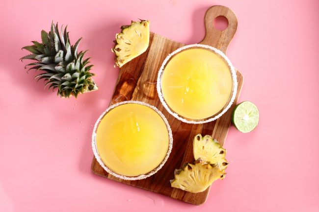Pineapple Mocktail in 2 Glasses on Cutting Board with Pink Background #recipes | Vitacost.com/blog