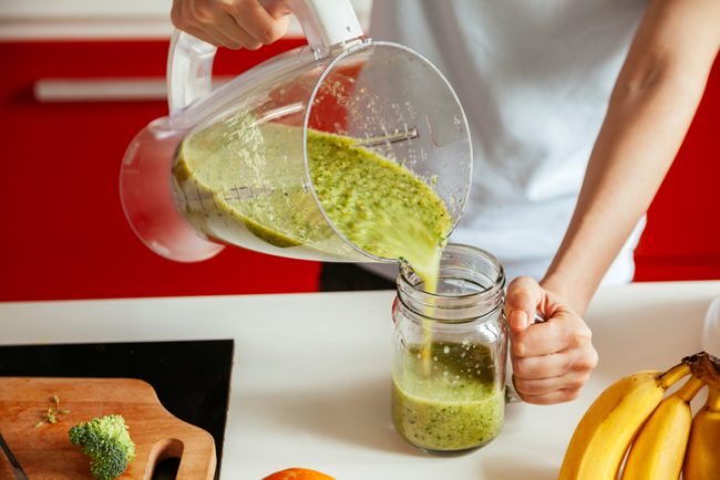 Woman Pouring Green Smoothie From Blender into Glass Jar on Countertop | Vitacost.com/blog