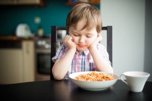 Boy Who is a Picky Eater Staring Grumpily at Bowl of Pasta on Table | Vitacost.com/blog