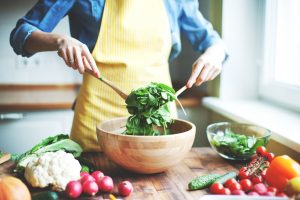 Woman Tosses Salad with Veggies on Wood Counter to with Collagen-Building Food | Vitacost.com/blog