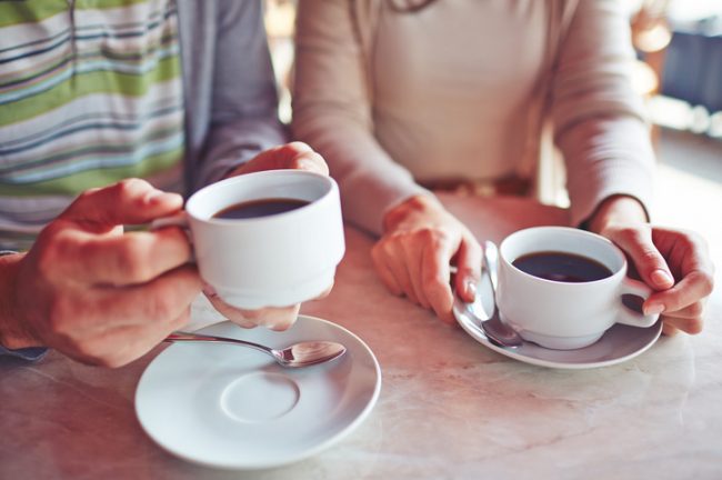 Couple Holding White Mugs Enjoying Coffee Health Benefits at a Diner | Vitacost.com/blog