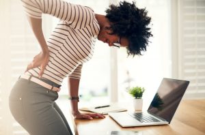 Woman Suffering From Stress and Inflammation Holding Back in Pain at Desk | Vitacost.com/blog