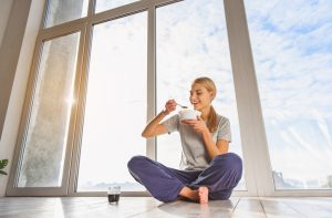 Woman Sitting on Floor in Front of Window Eating Oatmeal for Breakfast | Vitacost.com/blog