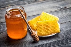The Benefits of Raw Honey, Pictured Here in a Jar with Honeycomb on Wood Table | Vitacost.com/blog