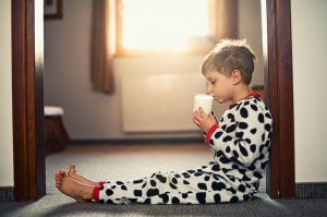 Child in Pajamas Sitting in Doorway Drinking Glass of Milk | Vitacost.com/blog