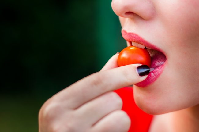 Close-up of Woman Eating a Cherry Tomato to Show the Best Foods for Skin, Hair & Nails | Vitacost.com/blog