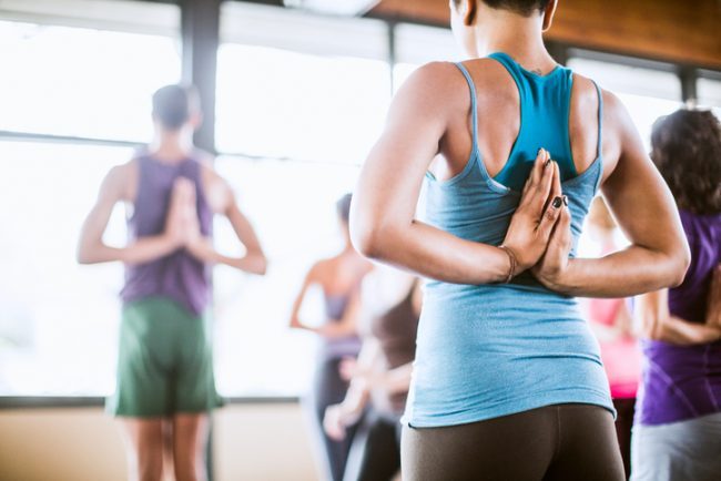 Yoga for Beginners: Types of Yoga Woman Holding Prayer Hands Behind Back in Group Yoga Class | Vitacost.com/Blog