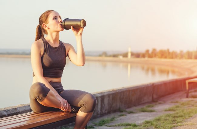 3 Benefits of Whey Protein Powder A Woman by a Lake Enjoys the Post-Workout Benefits of Whey Protein in Her Shaker Cup | Vitacost.com/blog