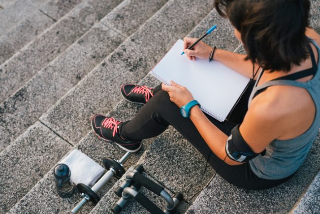 Woman Writing Down Her Fitness Resolutions for the New Year Female Athlete Sitting on Steps Writing Down Fitness Resolutions | Vitacost.com/blog
