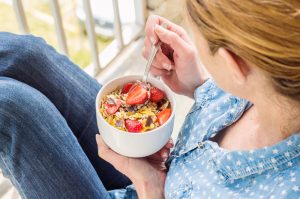 Woman on Balcony Eating Bowl of Cereal Loaded with Added Sugar | Vitacost.com/blog