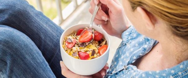 Woman on Balcony Eating Bowl of Cereal Loaded with Added Sugar | Vitacost.com/blog