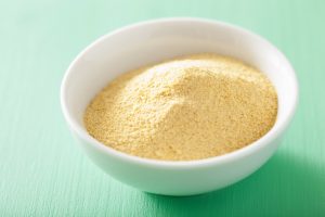 Bowl of Nutritional Yeast on Teal Background: Decipher the Facts from Fiction | Vitacost.com/blog