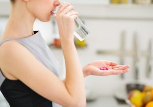 Side View of Woman Drinking Glass of Water While Taking Essential Vitamins | Vitacost.com/blog