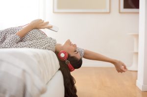Woman on Bed Taking Care of Ear Health by Listening to Music Quietly Through Headphones | Vitacost.com/blog