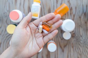 Open Hand Holding Several Vitamins and Supplements with Bottles Blurred in Background | Vitacost.com/blog